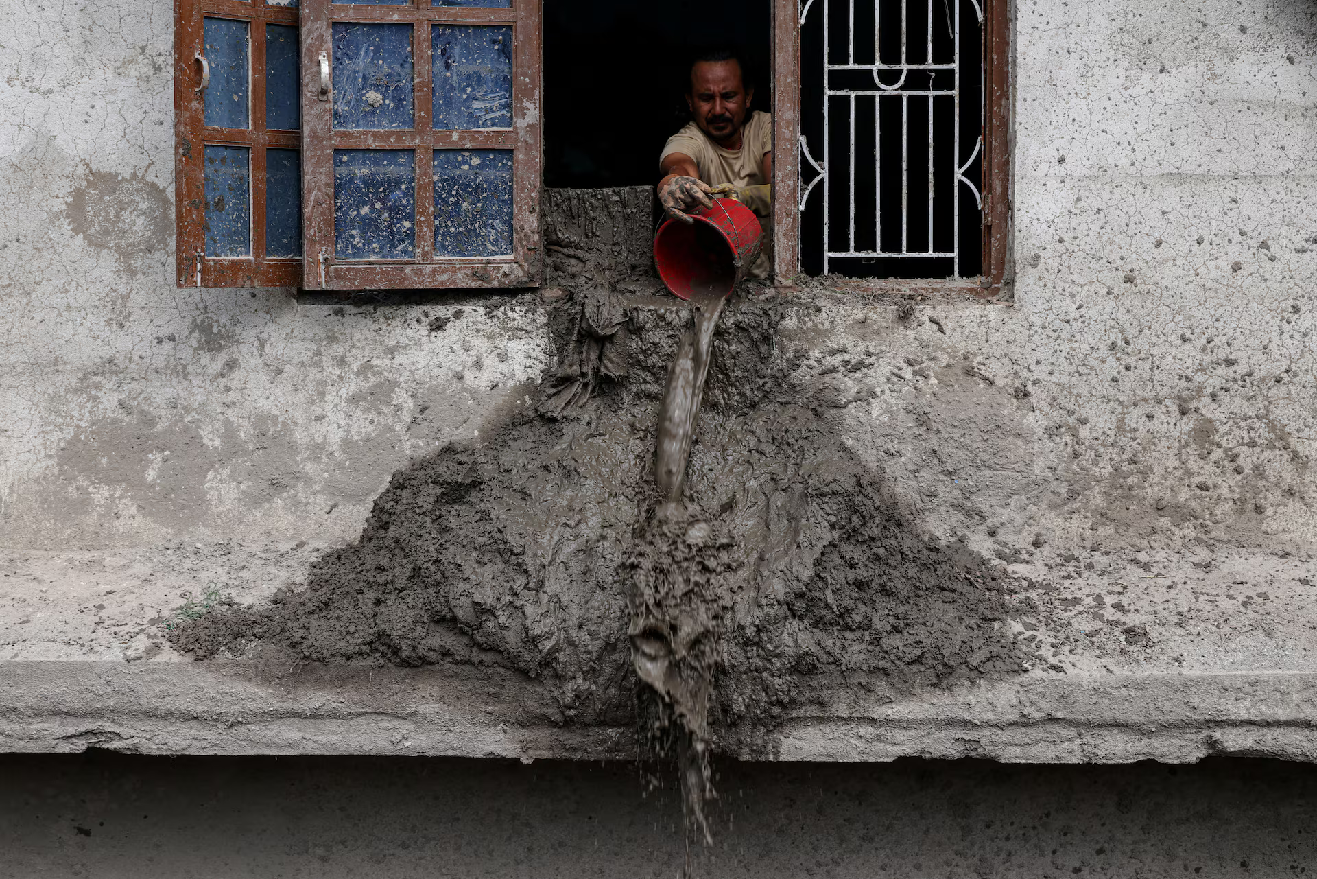 A man pours mud out of a window of a flood-damaged home.