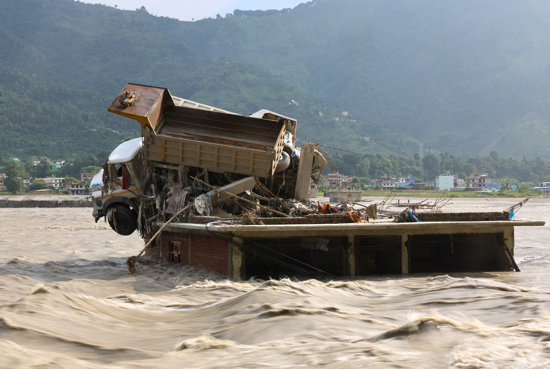 A flooded home, with damaged trucks on its roof.