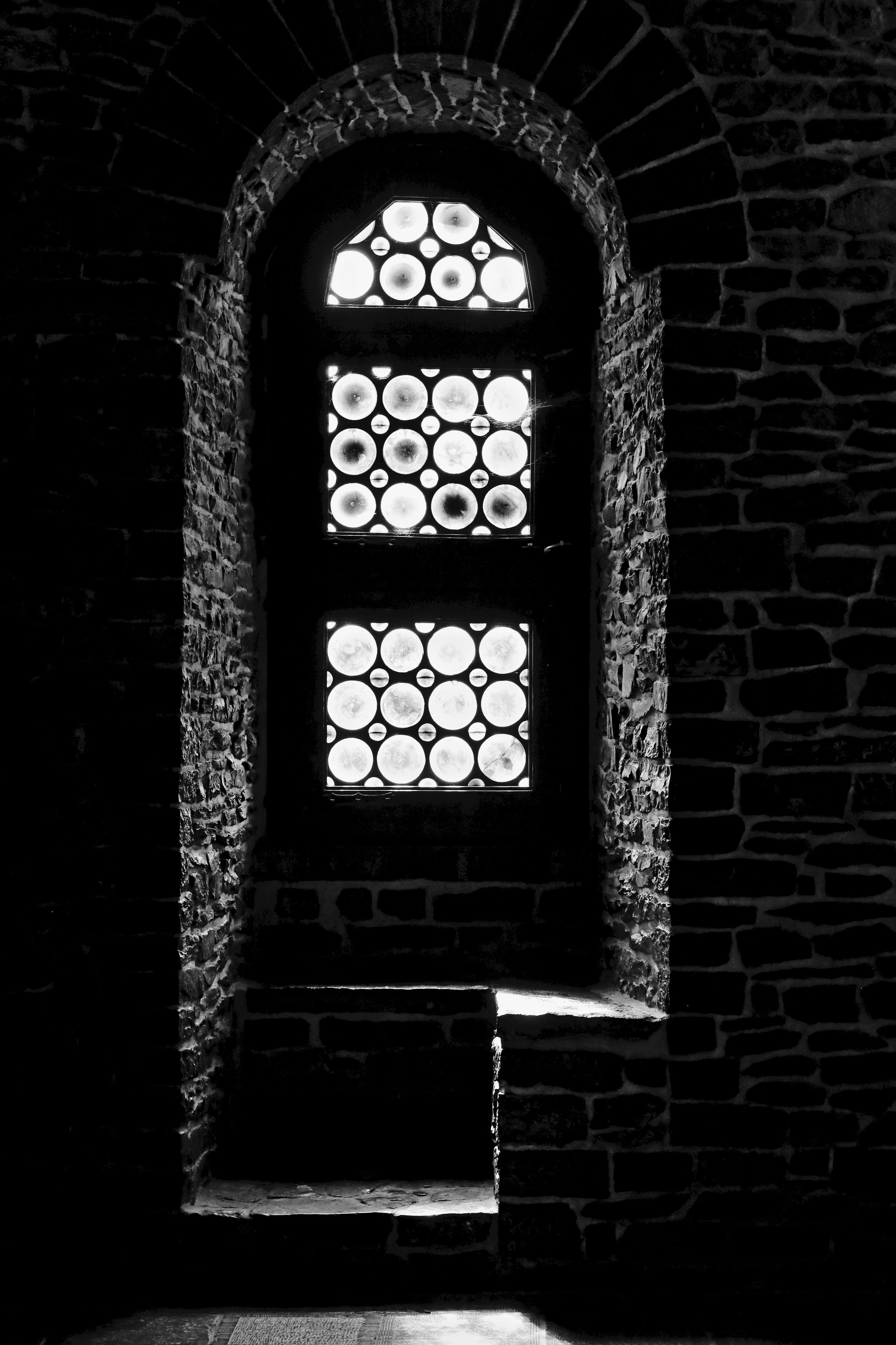 Schwarzweiss-Foto einer Fensternische in der Burg Gravensteen in Gent (Belgien). Das Fenster besteht optisch aus einzelnen runden Elementen. Sichtrichtung ist von innen nach aussen. Das Mauerwerk besteht aus einzelnen verschieden großen Steinen, die geglättet sind und zwischen den Steinen weiß verfugt.