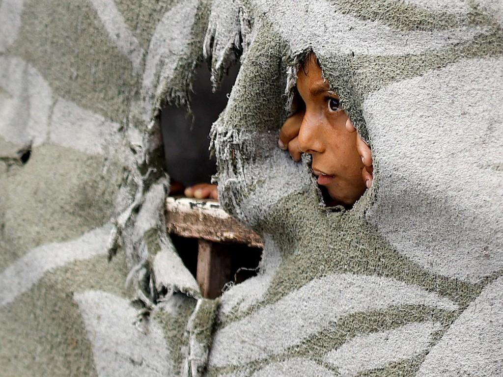 A Palestinian child looks out through a hole in a tent.