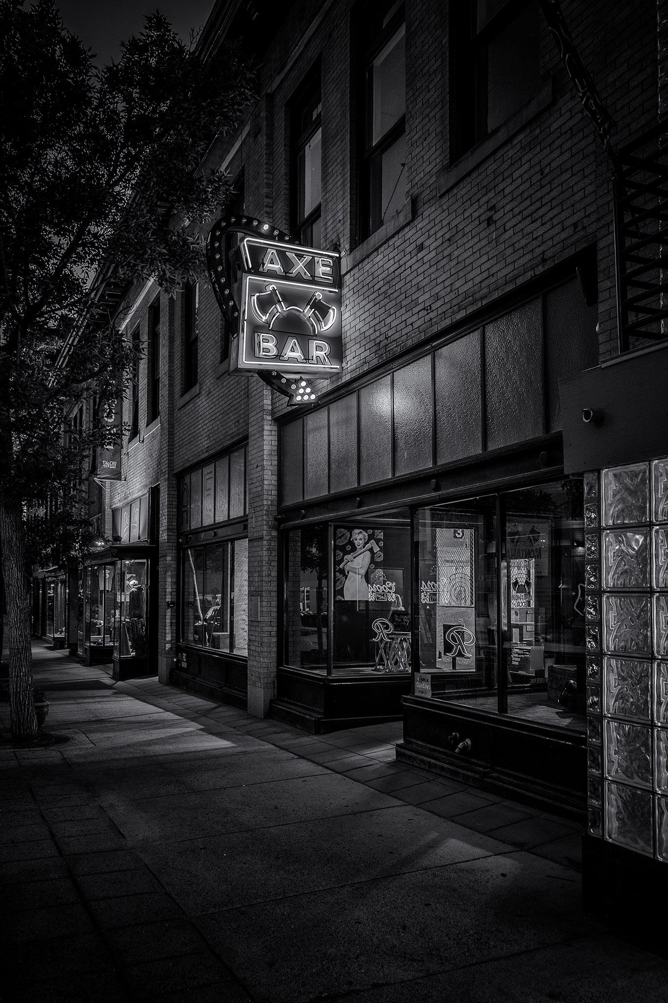 Axe Bar in Butte, MT by night. A neon sign of two crossed axes is glowing above the entrance.