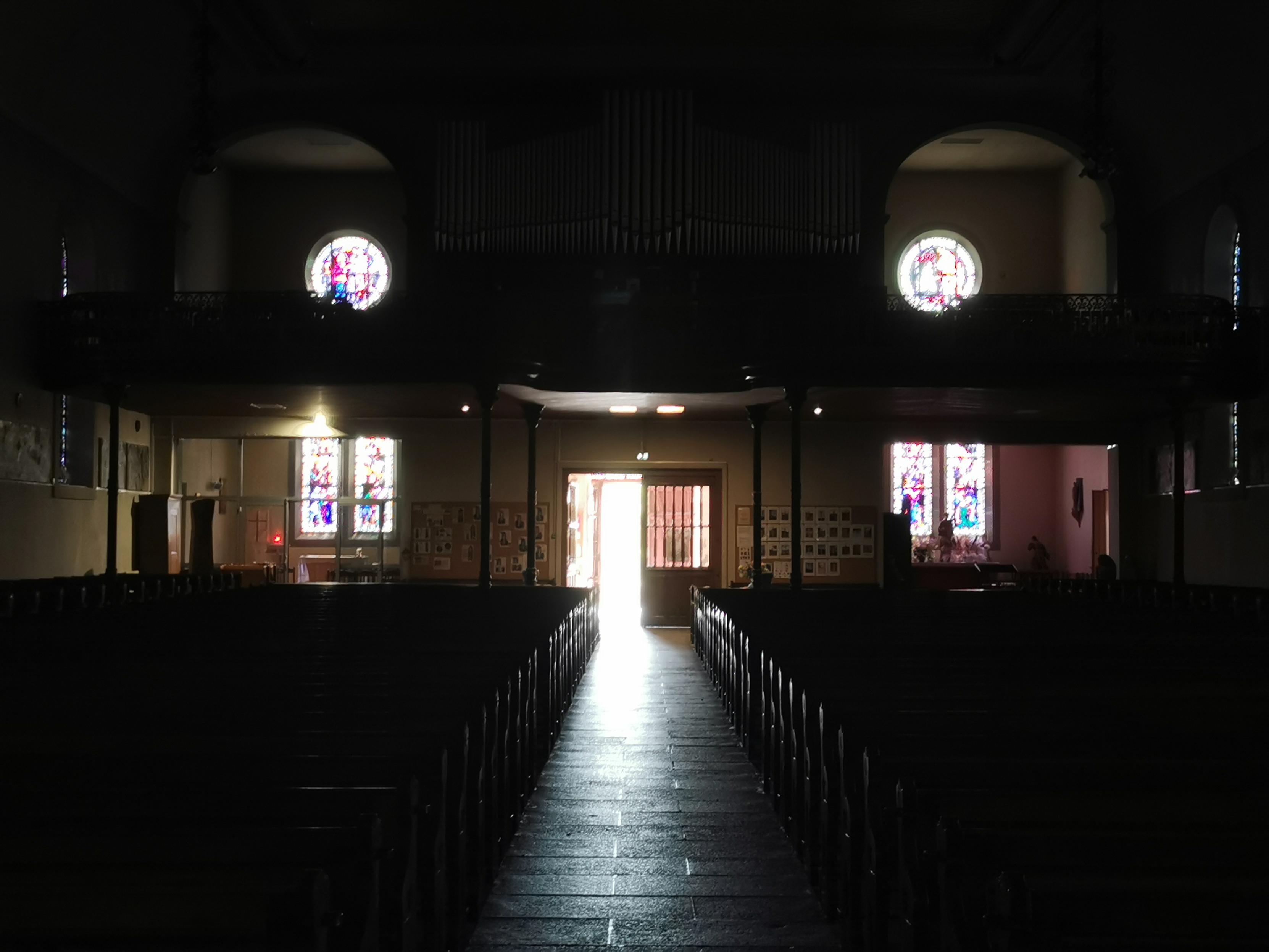 Vue de l'intérieur d'une église vers l'extérieur, ambiance sombre, ouvertures lumineuses.