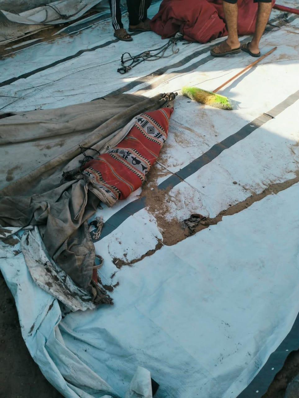 Large white tarps laid out on the ground with a red and black patterned cloth bundle and ropes.