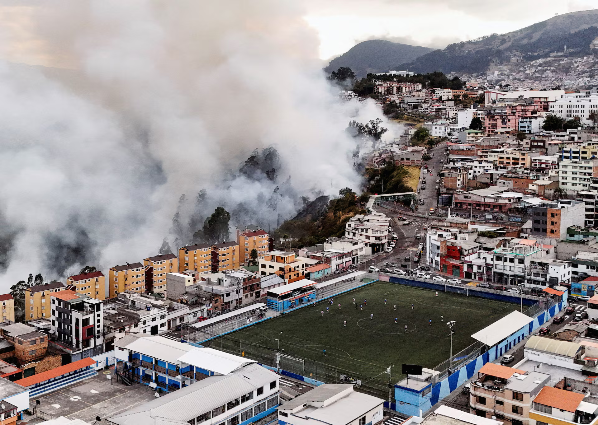 A football game goes on as fire & smoke approach.