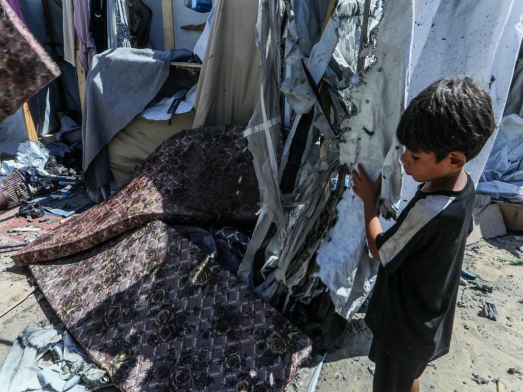 A displaced Palestinian boy inspects damage to a tent after an Israeli drone strike.