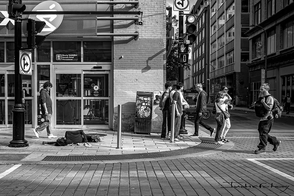 A man is lying on the sidewalk while people passing by don't even notice him.