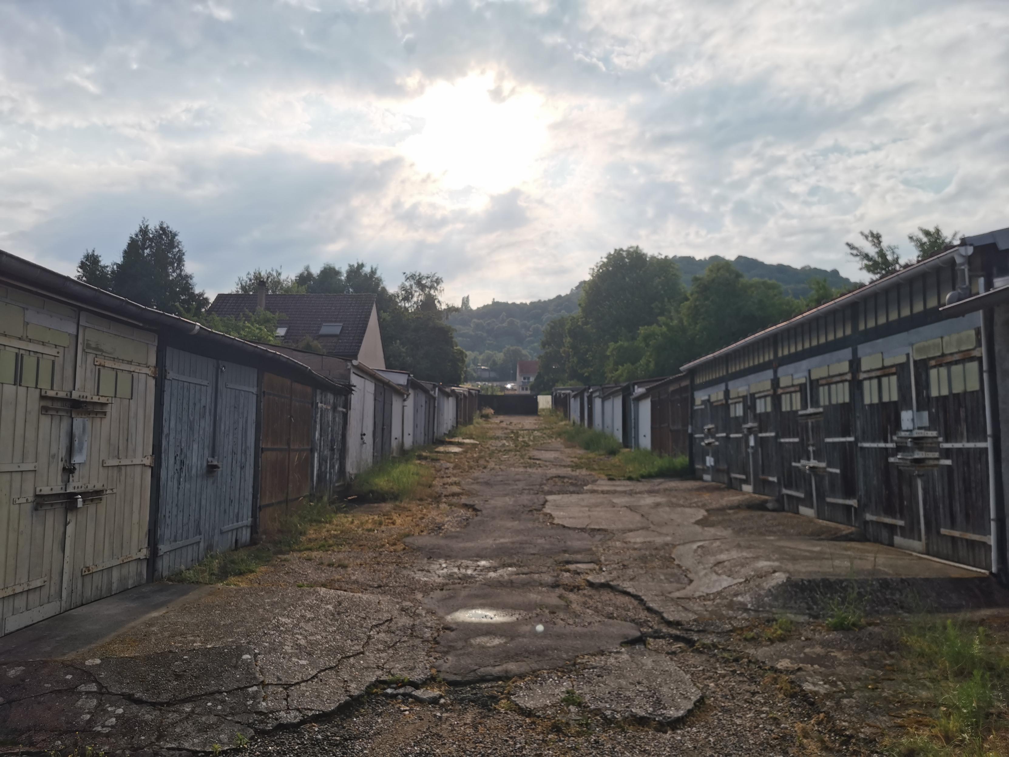 Allée défoncée entre deux rangées de garage sous un ciel étrangement voilé.
