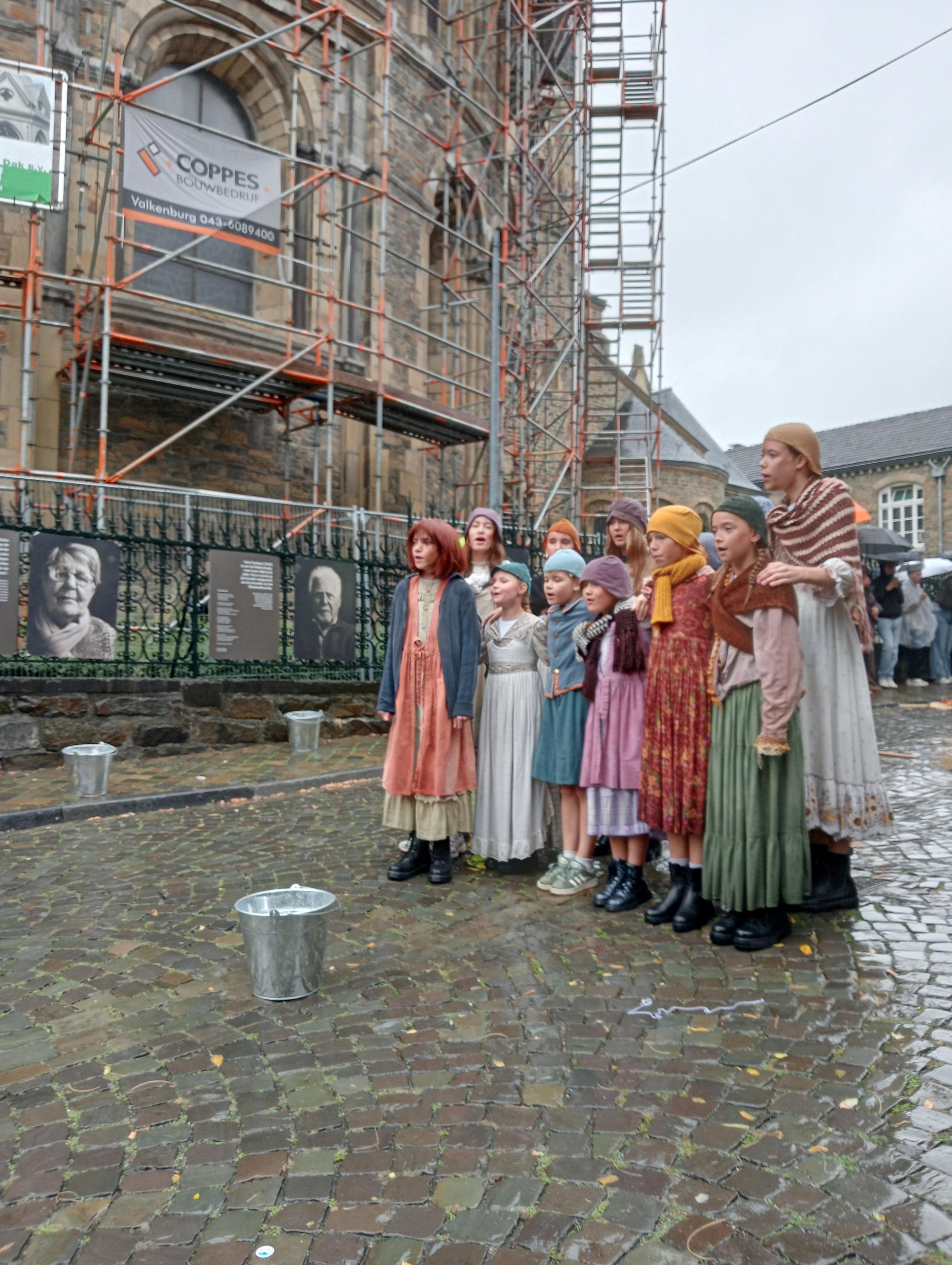 ichts aan het begin van de Stokstraat in Maastricht met aan de hekken van de Onze Lieve Vrouwe Basiliek twee zwart wit portretten gemaakt met wet plate collodion fotografie van oud bewoners Maria en Harrie die daar als kind opgroeiden en heel arm waren. Zij werden crapuul genoemd