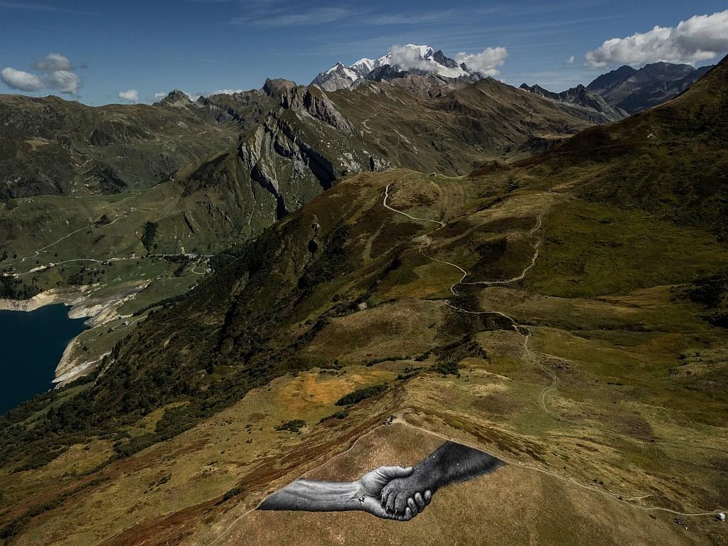 A giant fresco depicting a human hand clutching a dog’s paw on a mountain pasture.