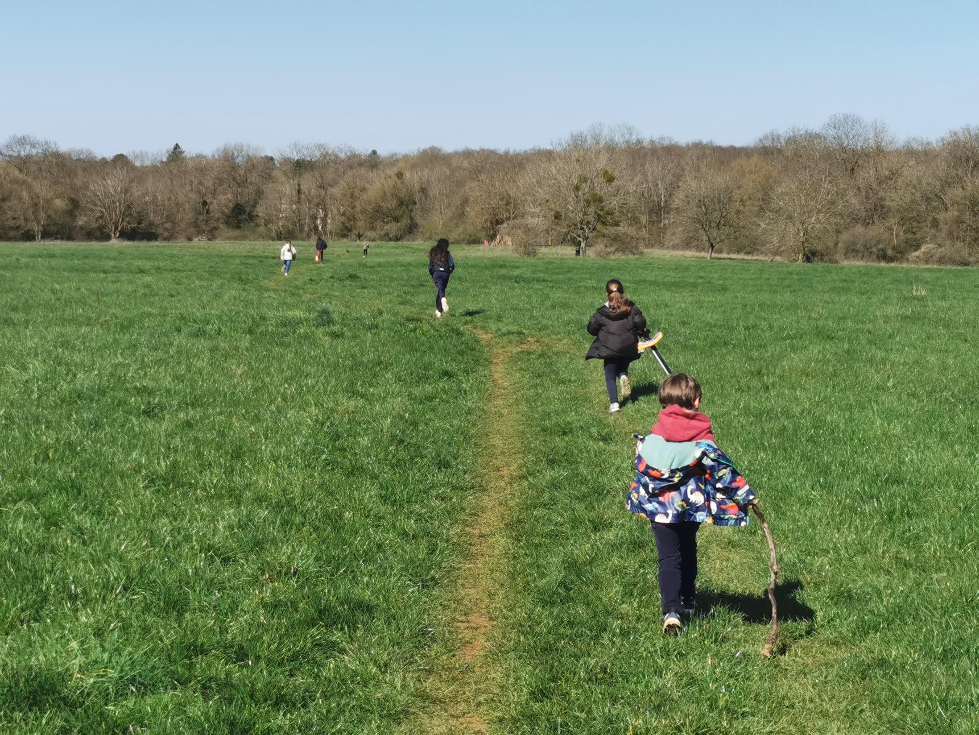 Un groupe d'enfants court dans une prairie traversée par un sentier.