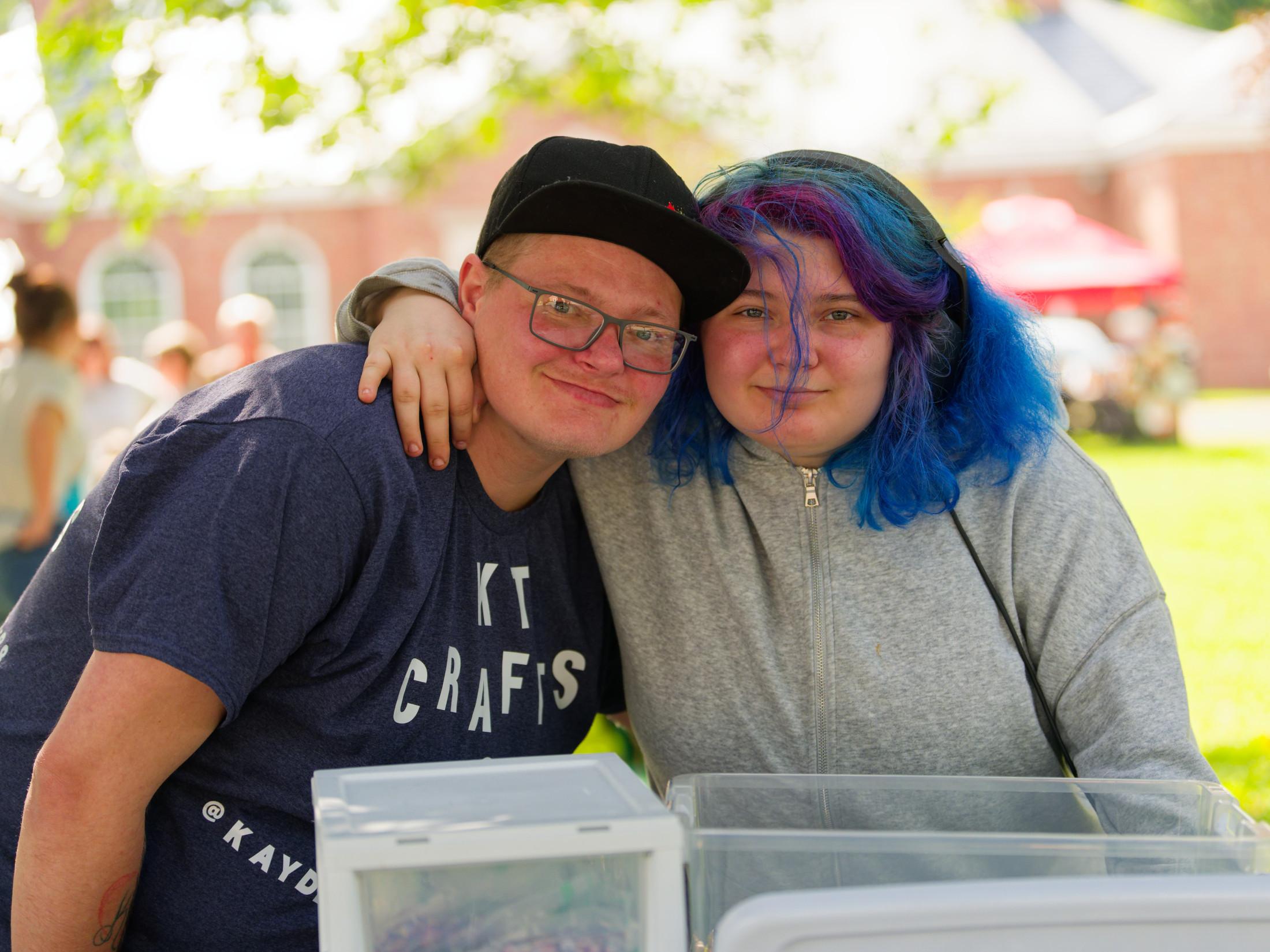 Man with dark shirt and baseball cap leans in towards woman with blue hair