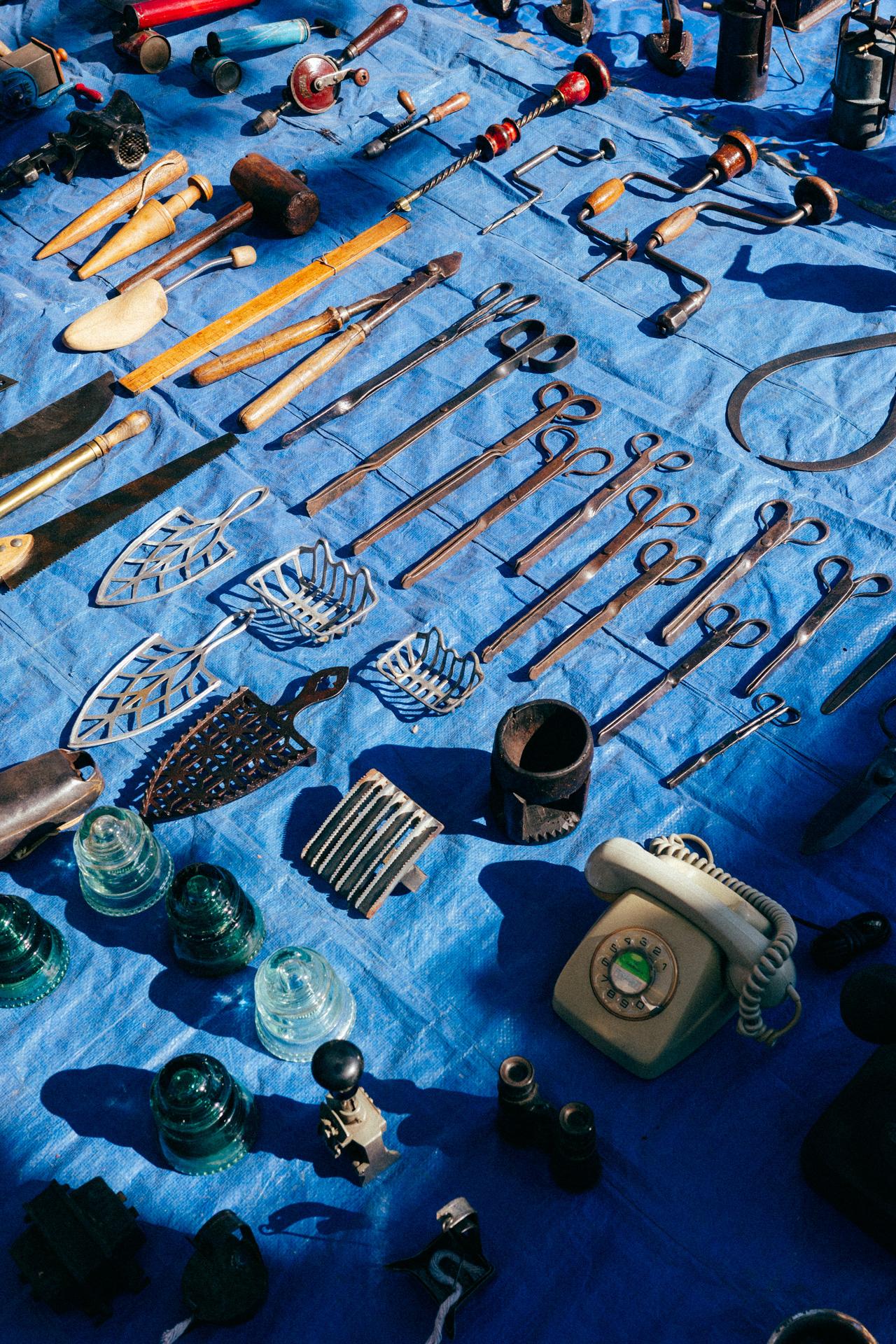 Fotografía de un puesto del mercadillo de Arenys de Mar lleno de herramientas y objetos curiosos.
Photograph of a stall at the Arenys de Mar flea market, filled with tools and curious objects.