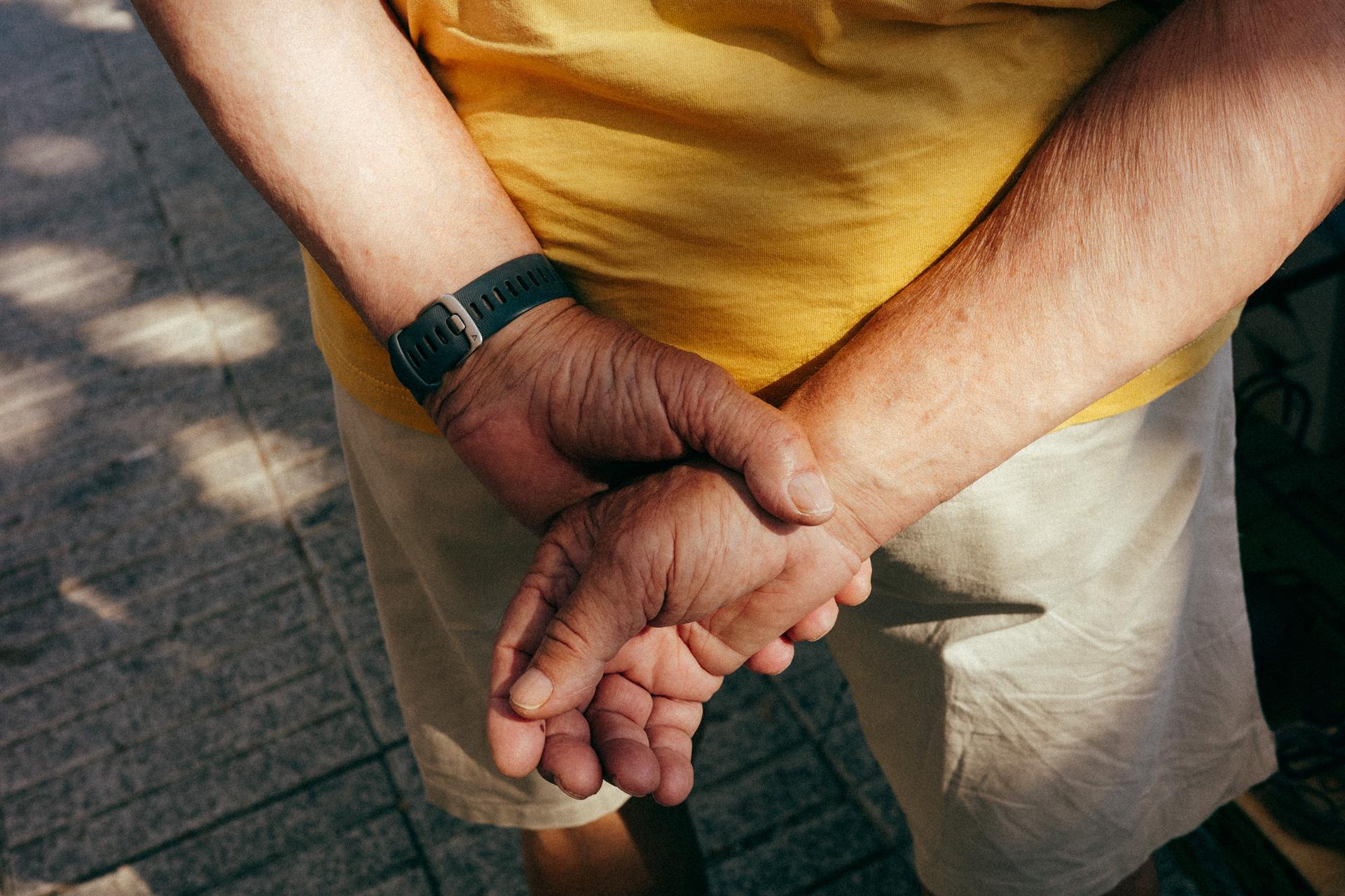 Fotografía detalle de las manos de una persona cruzadas a la espalda.
Close-up photograph of a person's hands crossed behind their back.