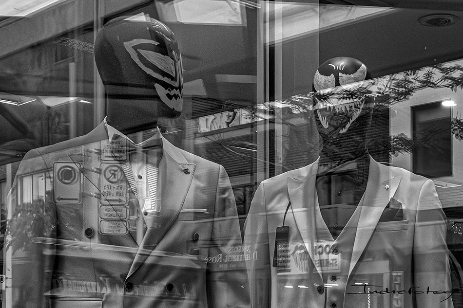 Two store display mannequins wearing "Lucha Libre" Masks, dressed in formal suits, with street reflections.