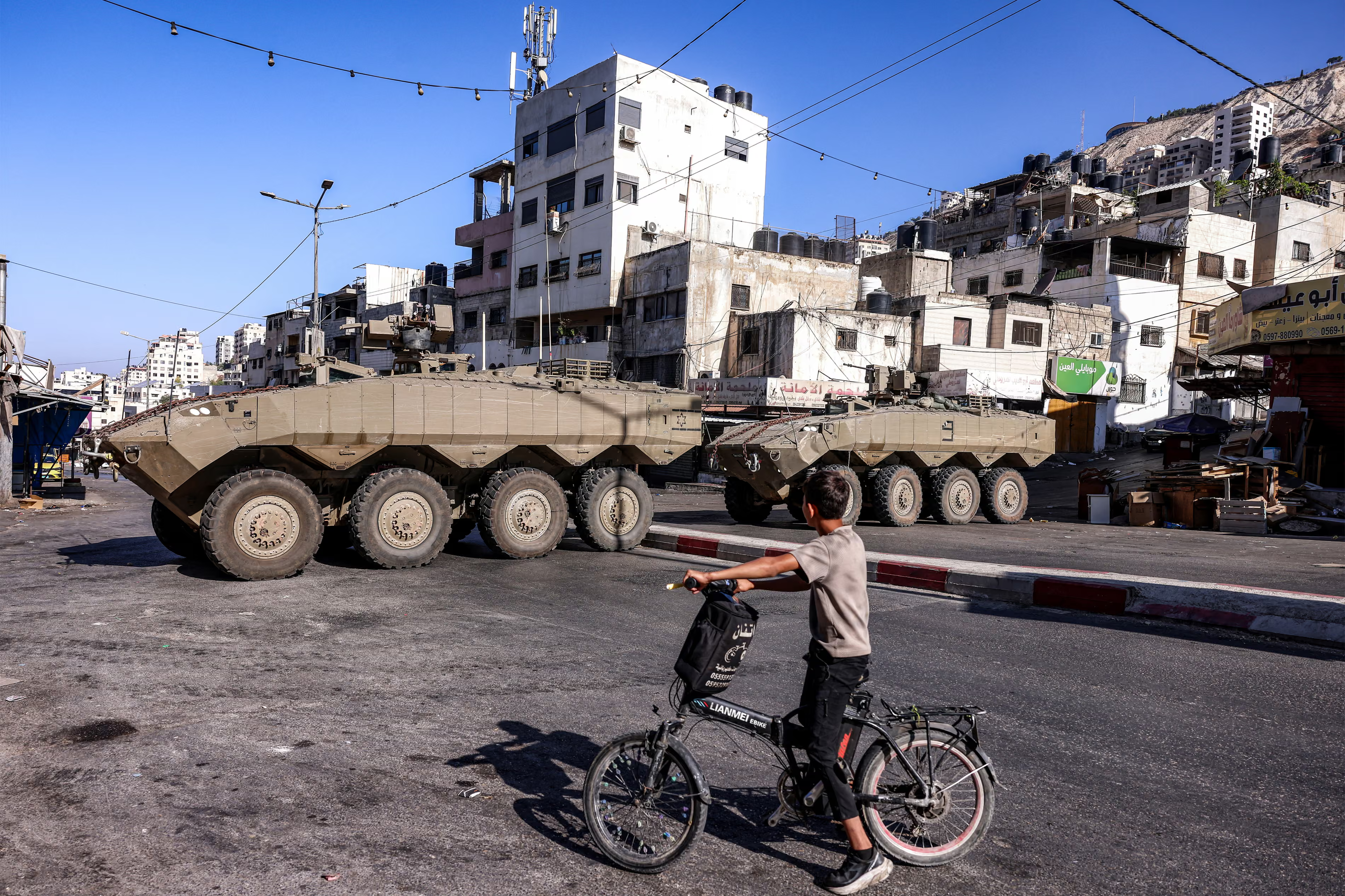 A boy cycles near Israeli armoured-personnel carriers.
