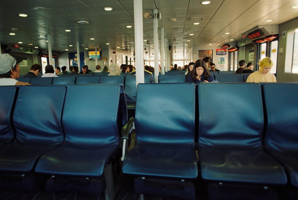 A row of empty blue seats in the foreground with people seated at others behind them. It's on the Seabus which connects the downtown to North Vancouver.
