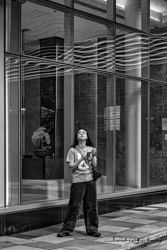A young woman looking up the sky wit her smartphone in hand.