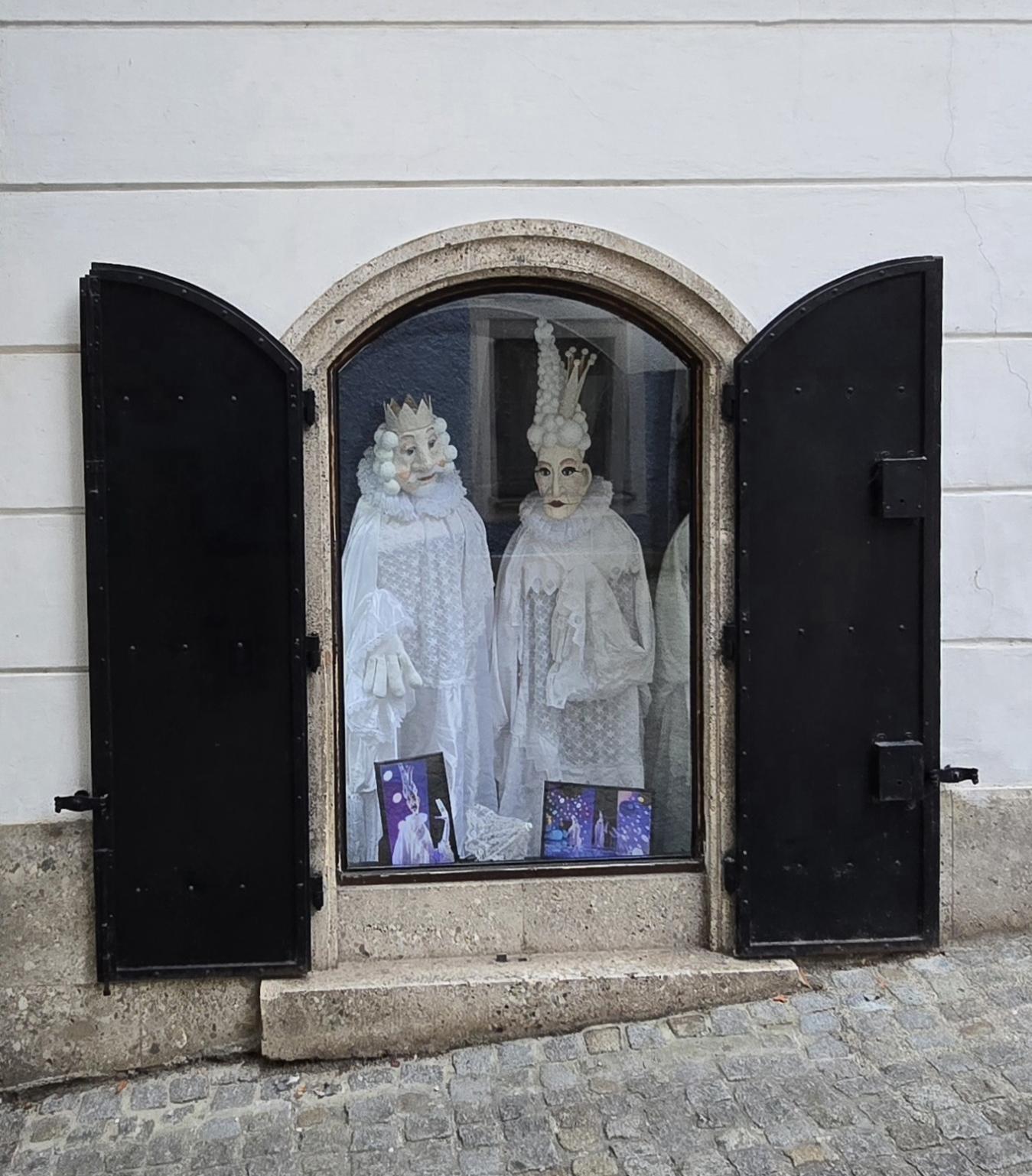 Schaufenster. Zwei Puppen für die Bühne in ganz weiß schauen heraus. Vermutlich König und Königin.