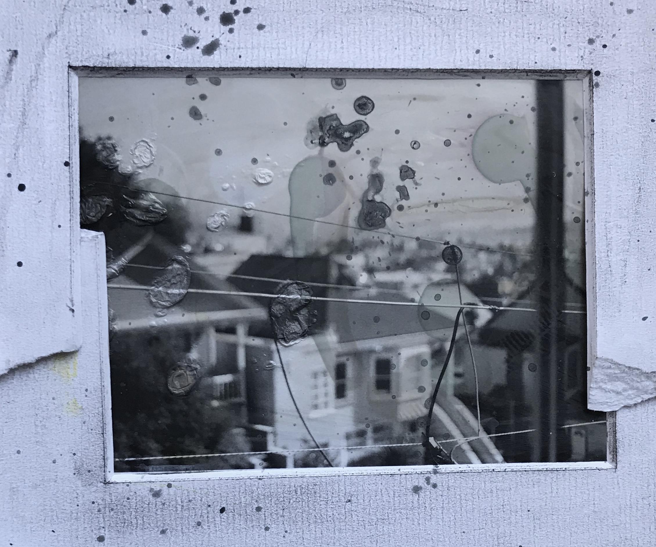 A view out a window of a 1920s house and landscape beyond. Thr house is blurry because the focus is on power lines outside the windows. It is collaged with torn, overlapping framing mattes around the outside. And the whole thing is spattered with ink and wax.
