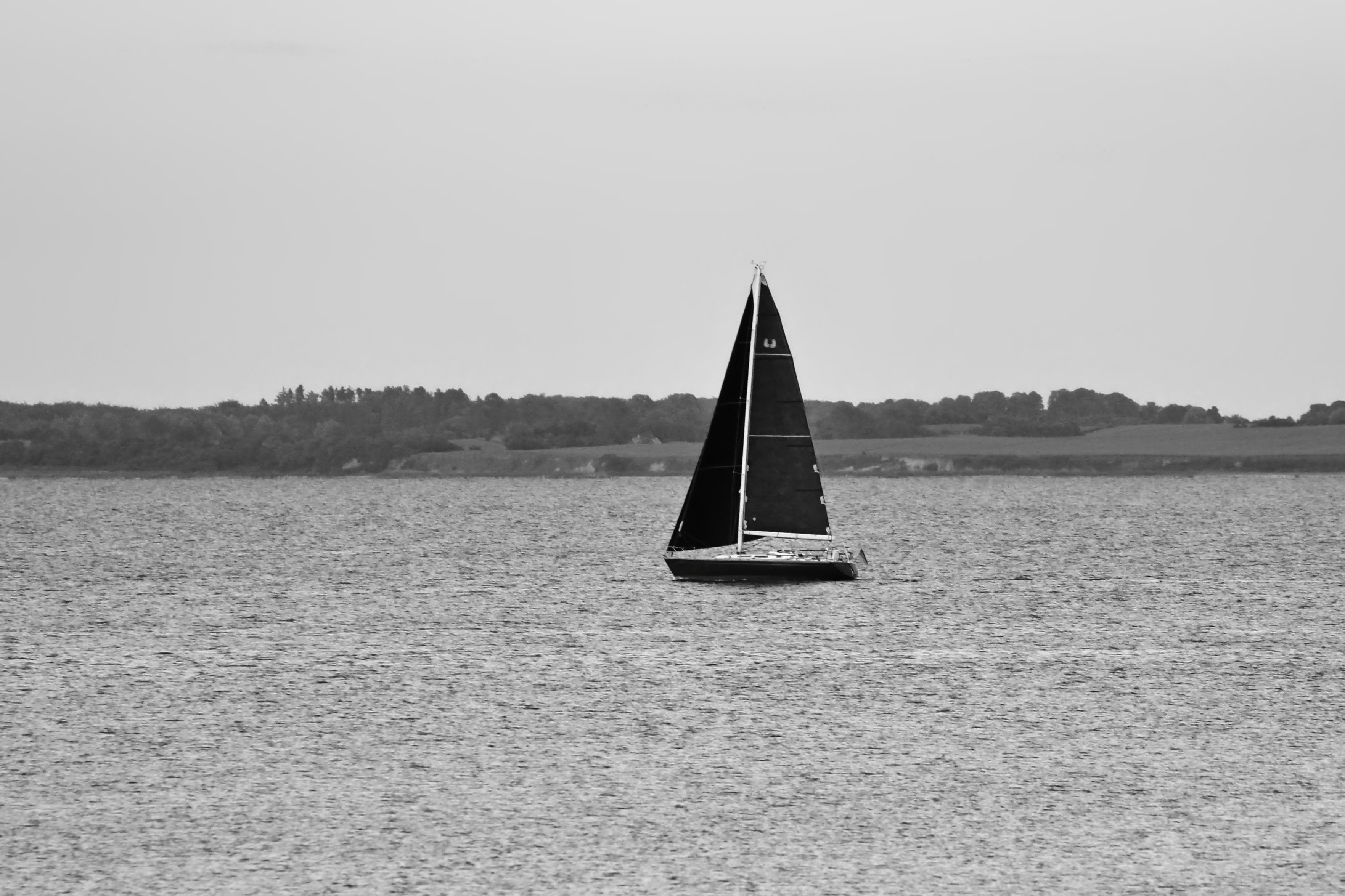 Schwarzweiss-Foto eines Segelbootes mit schwarzen Segeln und schwarzem Rumpf vor der Küste der dänischen Insel Langeland auf der ruhigen Ostsee.