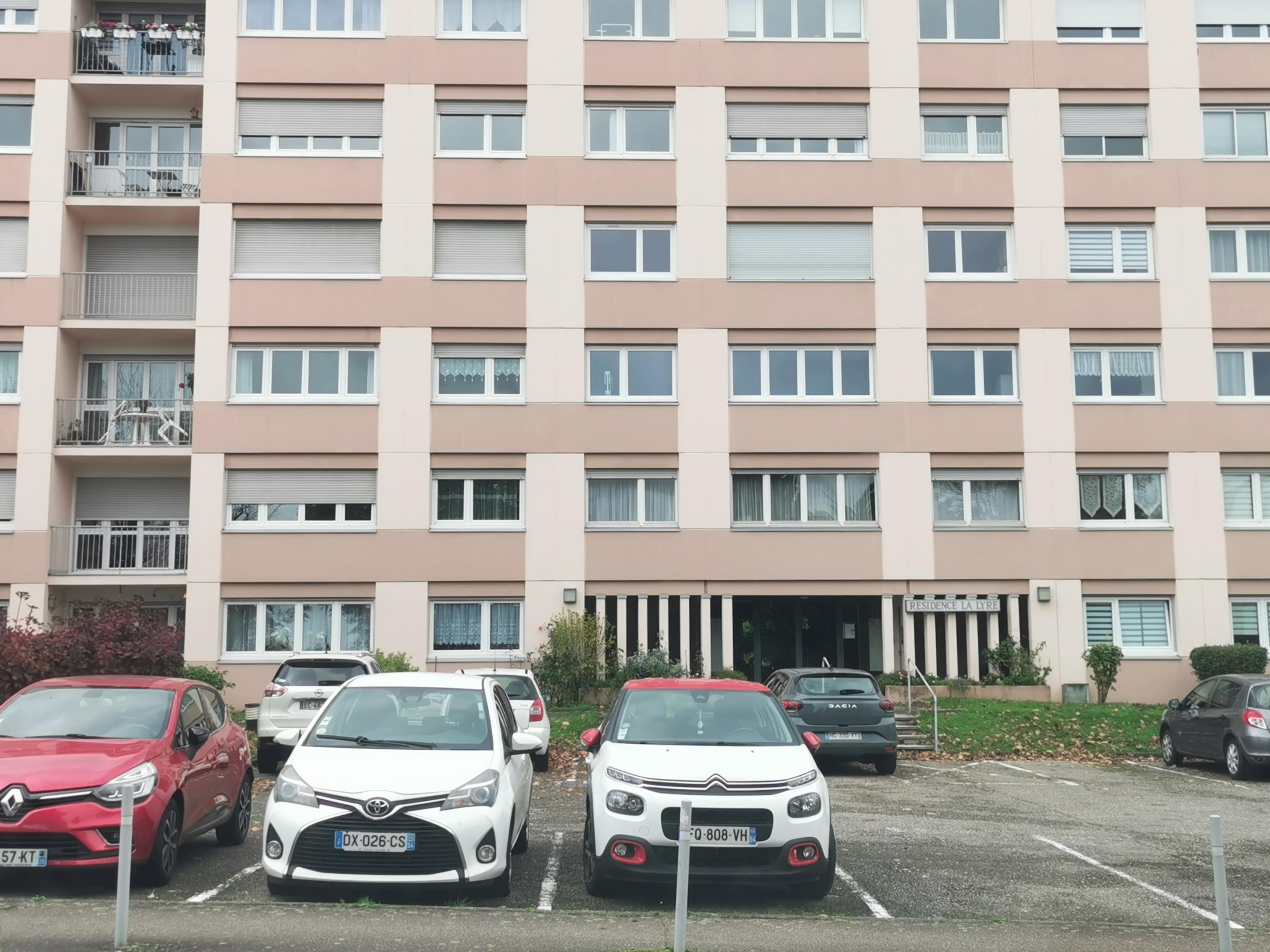 Façade frontale d'un immeuble résidentiel devant lequel sont garées des voitures.