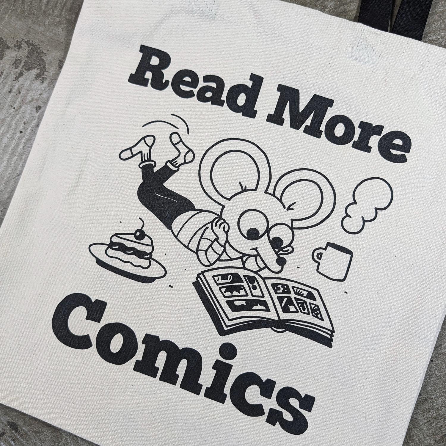 Close-up of tote Bag with black handles. A cartoon mouse reads a comic. A large text reads "Rad More Comics"