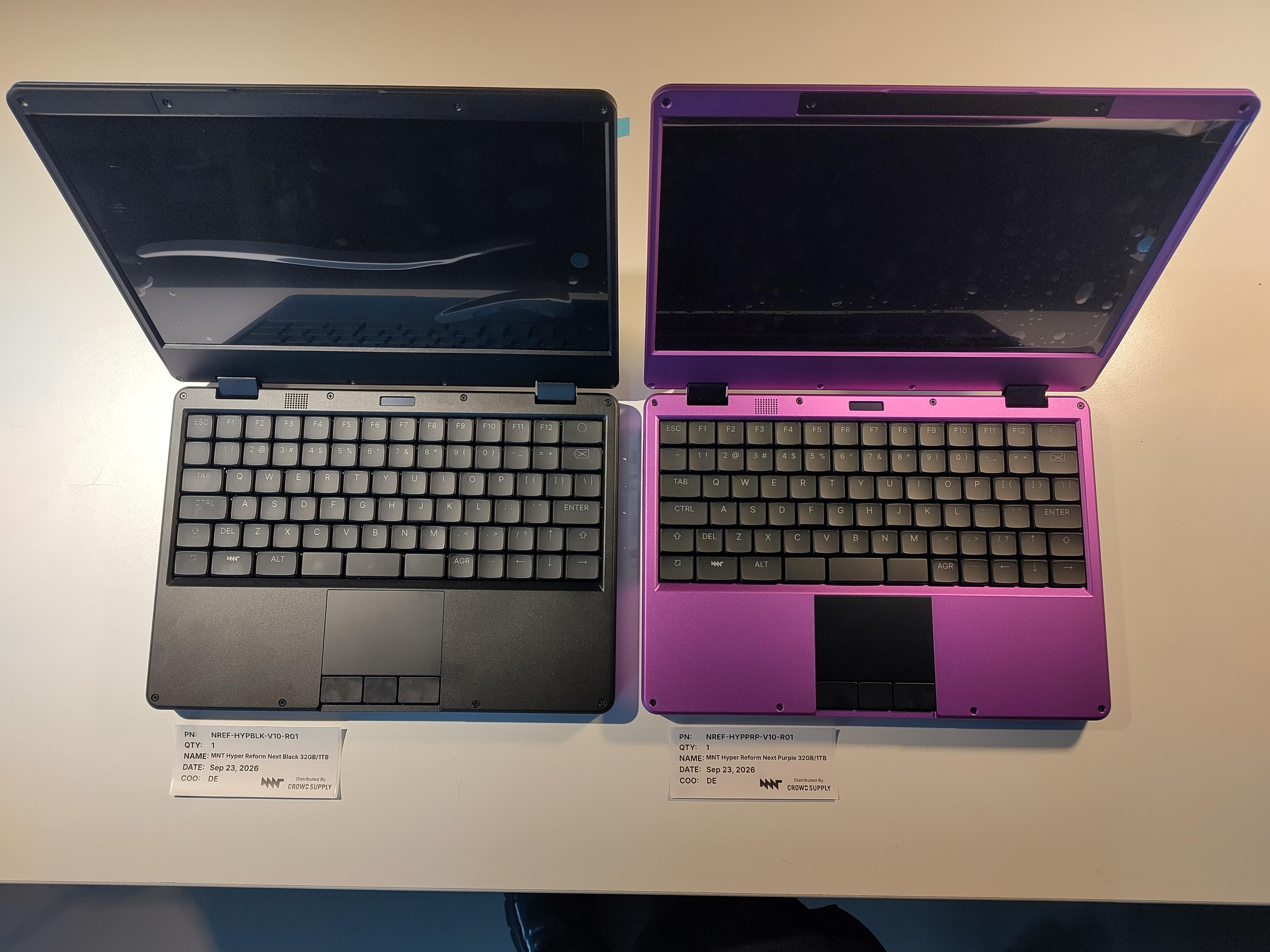 a black hyper reform next and a purple hyper reform next on a white table surface, shot from above. the displays still have protective foil on them.