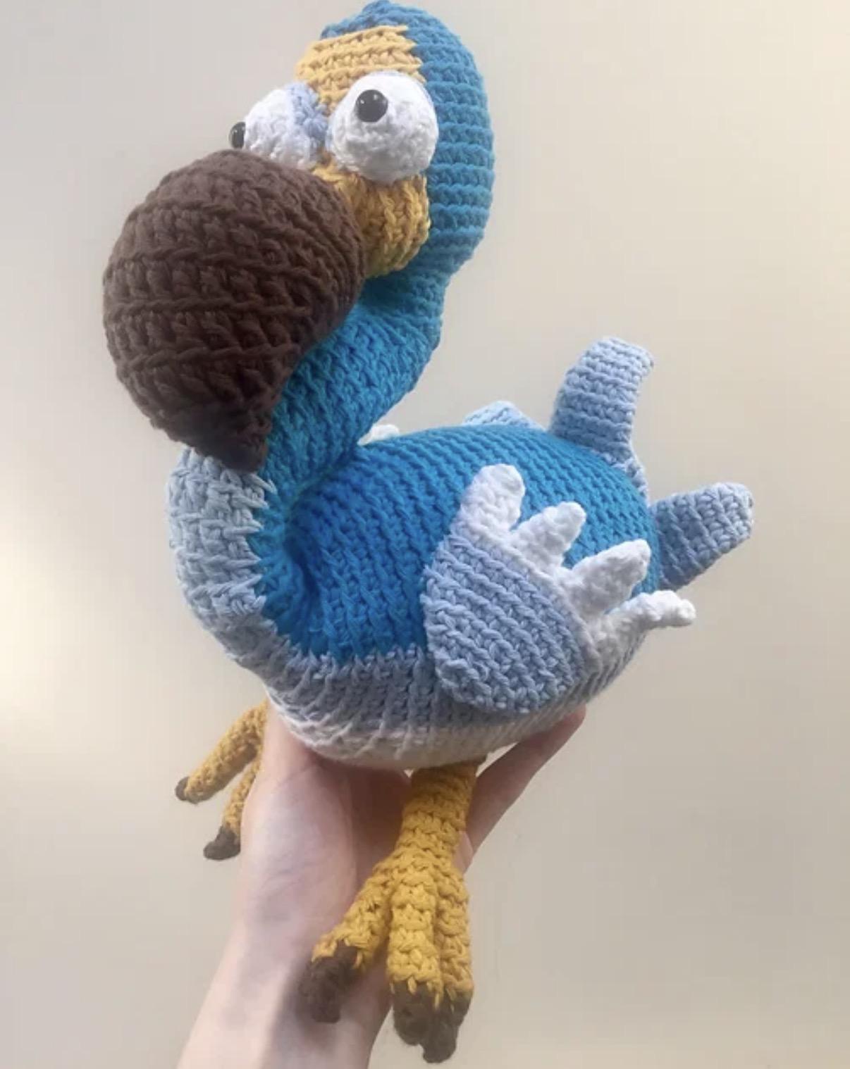 A crocheted stuff toy of a very wonky looking (deliberately) rotund bird with blue and white plumage, a bulbous brown beak and bulging eyes 