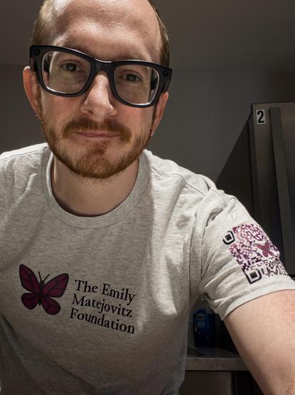 A man wearing black glasses and a grey t-shirt with a purple butterfly and text: "The Emily Matejovitz Foundation"

The t-shirt has a purple and white pattern on the sleeve. 