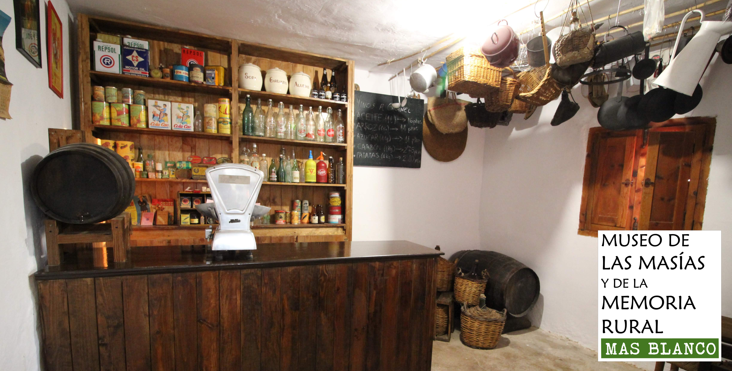 Cartel del Museo de las Masías y de la Memoria Rural donde se muestra una de las instancias. En este caso es la tienda donde se ven productos del siglo pasado en una estantería, un mostrados y una balanza.