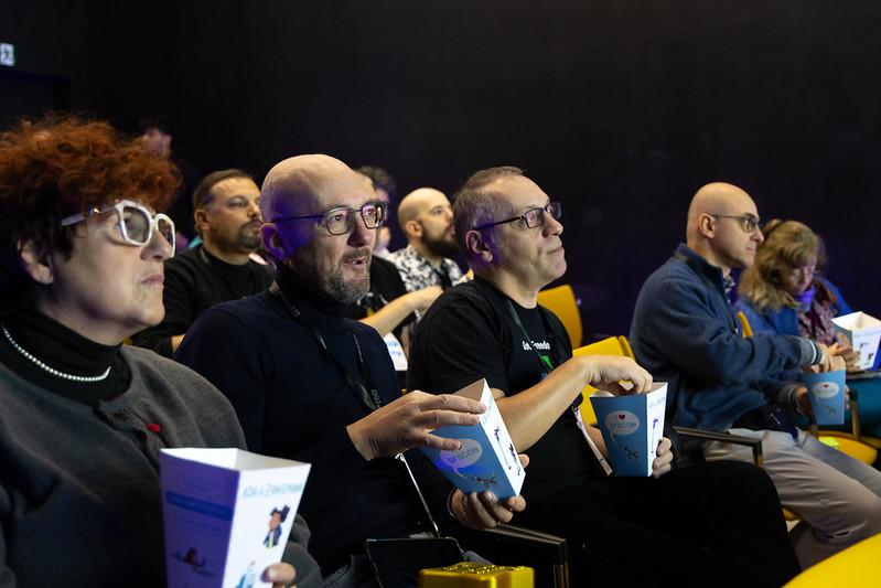 People sitting in a seminar room at SFSCON watching a presentation, holding popcorn boxes.