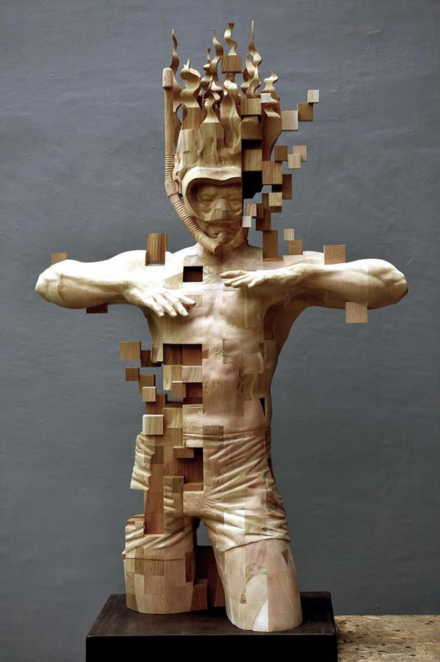 A wooden sculpture of a athletic man wearing a diving mask and snorkel. The sculpture is composed of pixelated wooden blocks that appear to break away from his body and hair, creating a digital pixelation effect.