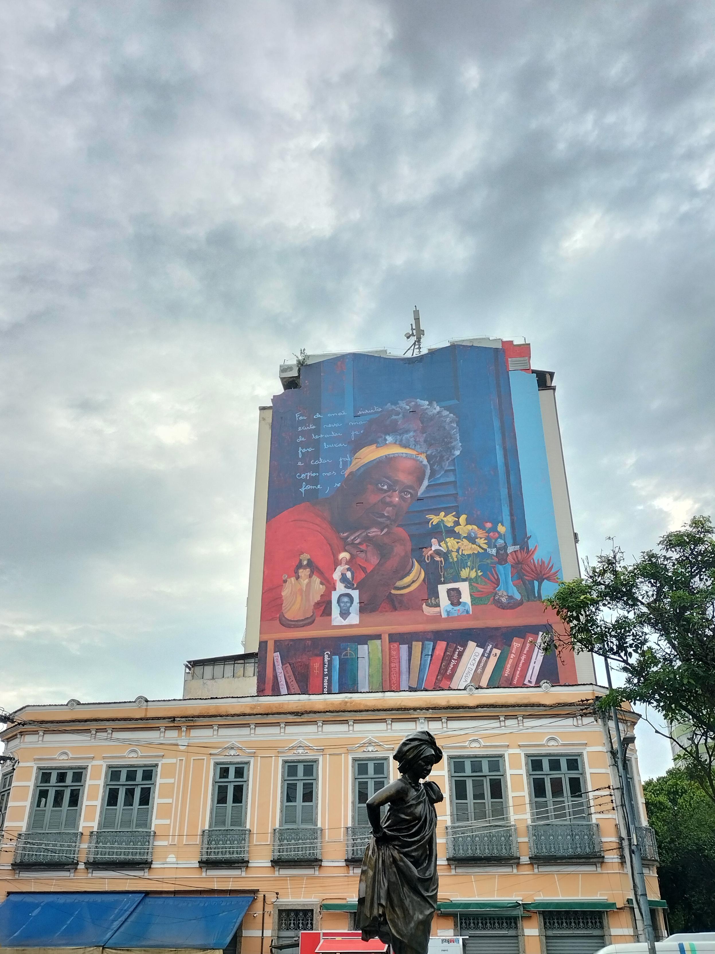 Resistencias africanas.Mural de la escritora negra Conceição Evaristo, con ella, una cita que no se lee,altar con la mezcla de orishas y santería católica y estantería de libros con sus títulos.Debajo,estatua cortada de la primera mujer negra con turbante y ropa atada que triunfó en Europa por mezcla de danza contemporánea y danza influencia africana,volvió a Brasil y fundó su compañía (no recuerdo su nombre)