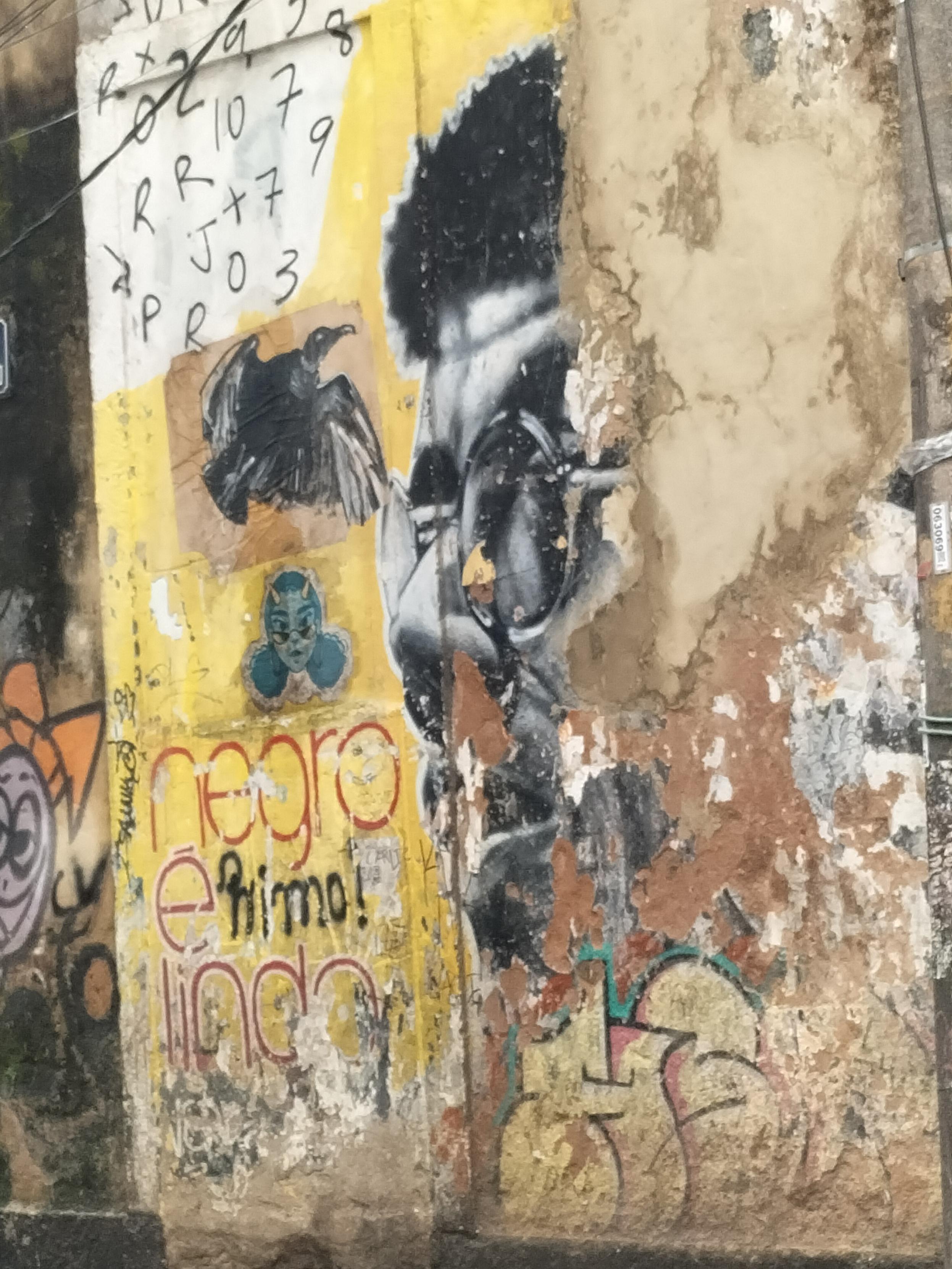 Mezcla de grafitis:pajaro negro en vuelo,mujer azul con cuernos y gafas negras,letras rojas negro é lindo y rostro de persona negra con gafas de sol (deteriorado)