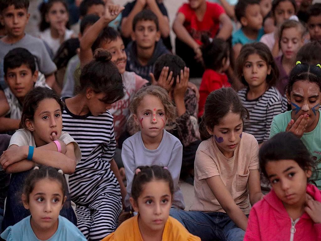 isplaced Palestinian children watch a film at a makeshift open-air cinema.
