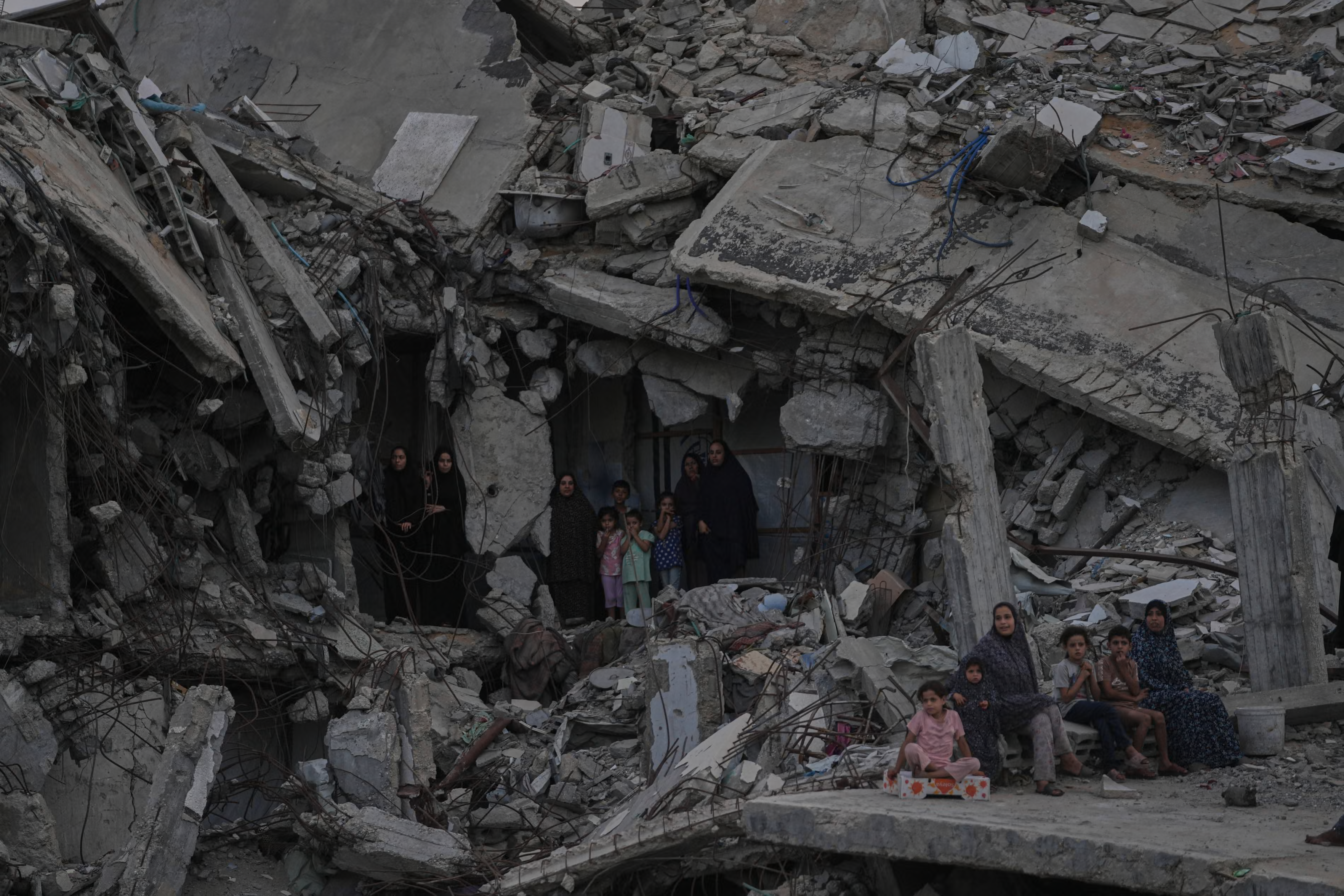 Palestinian women and children watch a strongman championship from among the rubble of destroyed buildings.