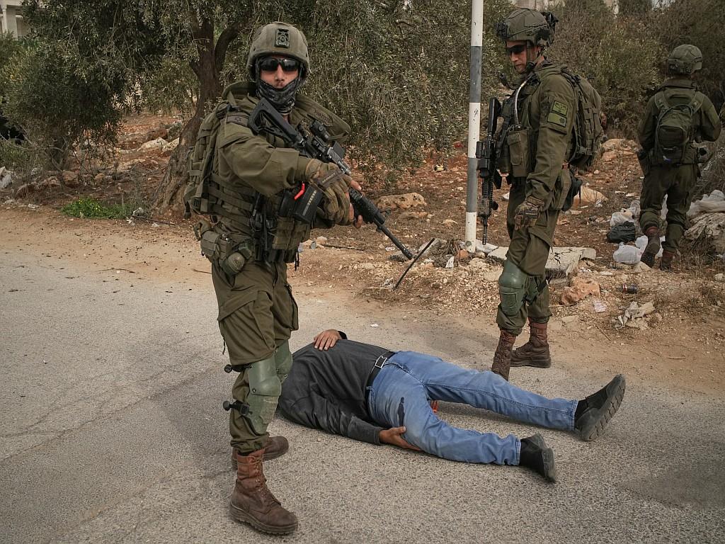 Israeli soldiers stand beside a wounded Palestinian man lying on a road after they shot him following a settler attack on Palestinians harvesting olives.

... in the latest violent attempt to prevent Palestinians from harvesting olives on their own land.