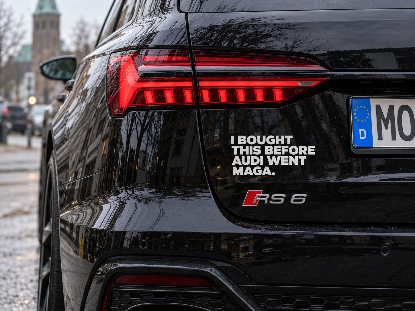 KI-generiertes, fotorealistisches Bild: Nahaufnahme des Hecks eines schwarzen Audi RS6 Avant auf einer nassen Straße in Moers. Die roten LED-Rückleuchten leuchten, im unscharfen Hintergrund sind Gebäude und ein Kirchturm zu erkennen.
Auf der schwarzen Heckklappe steht in großen, weißen Großbuchstaben:
„I BOUGHT THIS BEFORE AUDI WENT MAGA.“
Auf Deutsch: „Ich habe dieses Auto gekauft, bevor Audi zu MAGA überging.“
Der Schriftzug ist eine satirische Anspielung auf die bekannten Tesla-Aufkleber